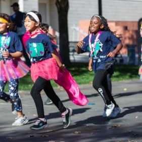 Girls on the Run participants smile while running at the Fall 2021 5K in tutus and capes.
